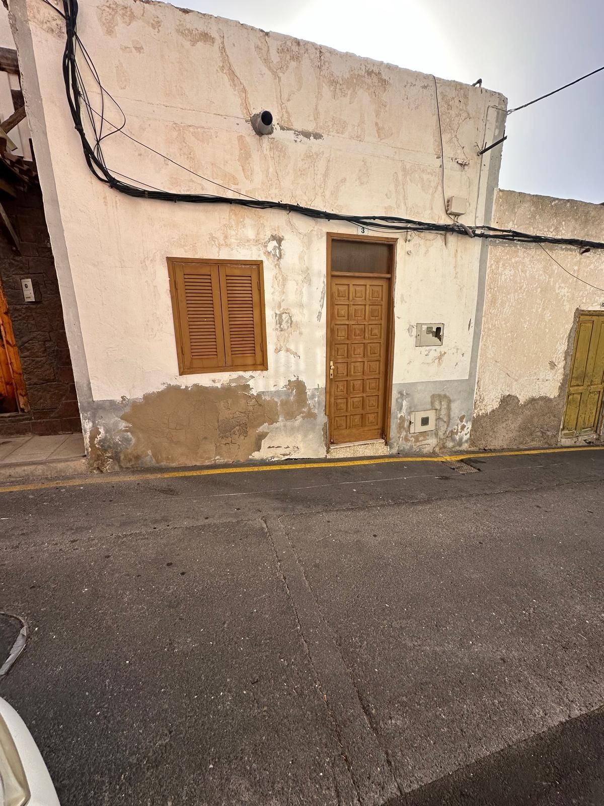 Old building with cracked walls, wooden door, and window on a narrow street.